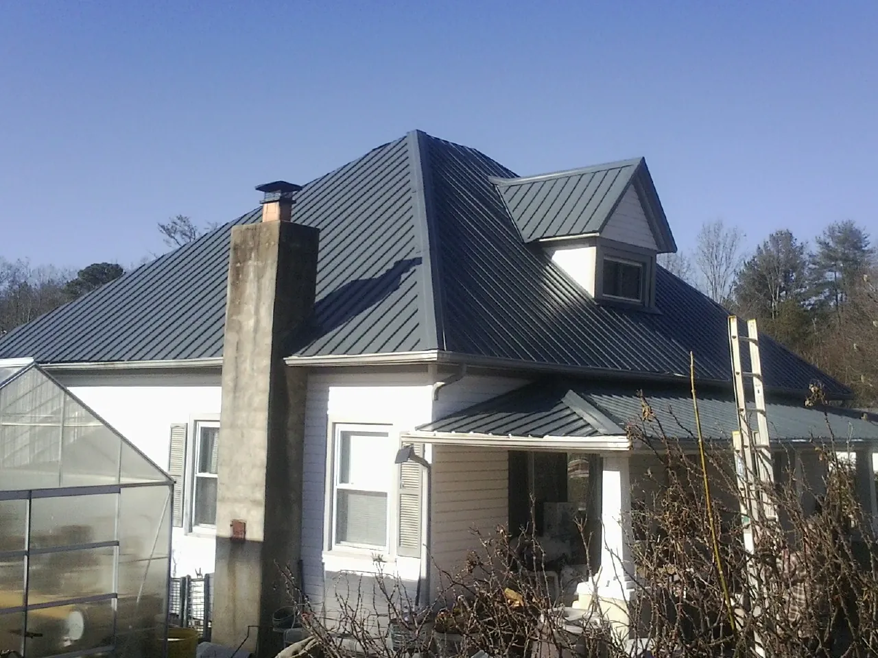 Dark blue standing seam metal roof on a white farmhouse with dormer — Slate & Tile Roof Repair by Roofing Brothers in Ansonville
