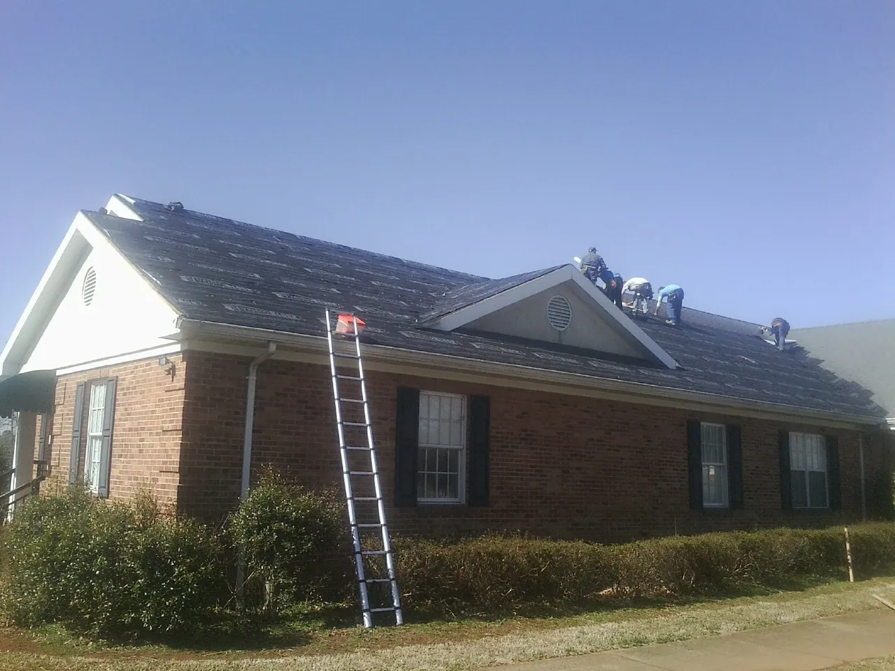 Crew tearing shingles off a brick ranch roof with a ladder set — Emergency Roof Repair work by our crew in Ansonville