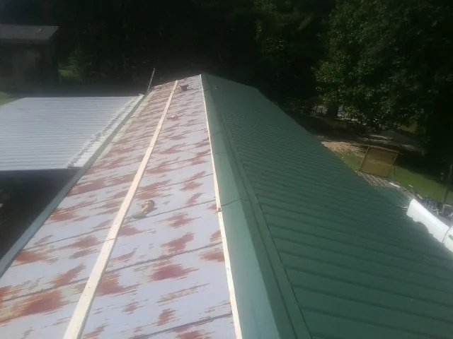 Old rusted panels beside newly installed green metal roofing — Wind Damage Roof Repair by Roofing Brothers in Ansonville