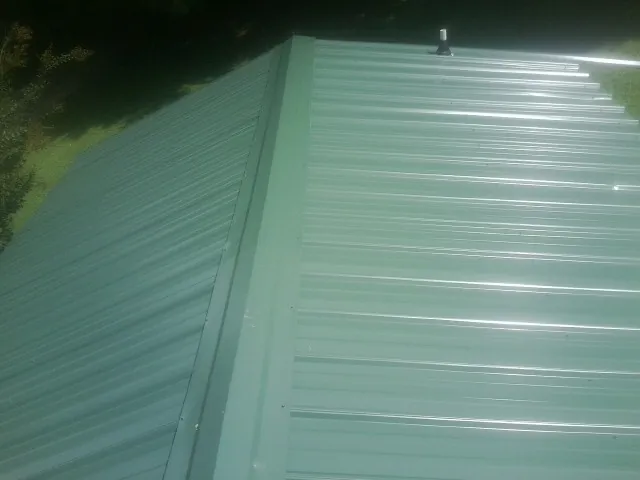New green metal panels meeting at the ridge of a roof — Flat Roof Repair work by our crew in Ansonville