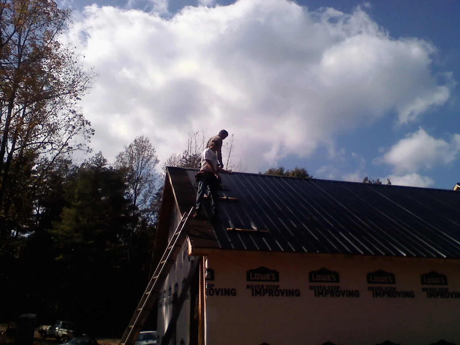 Roofer fastening dark metal panels high against a cloudy sky, from a Roof Inspection job in Ansonville