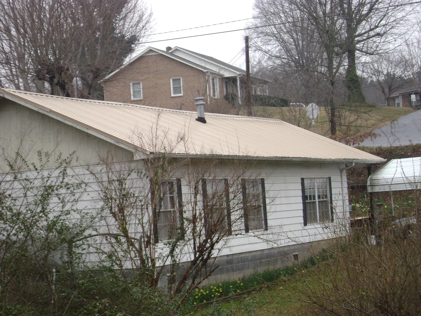 Tan metal roof on a white sided house set into a hillside — Commercial Roofing by Roofing Brothers in Ansonville